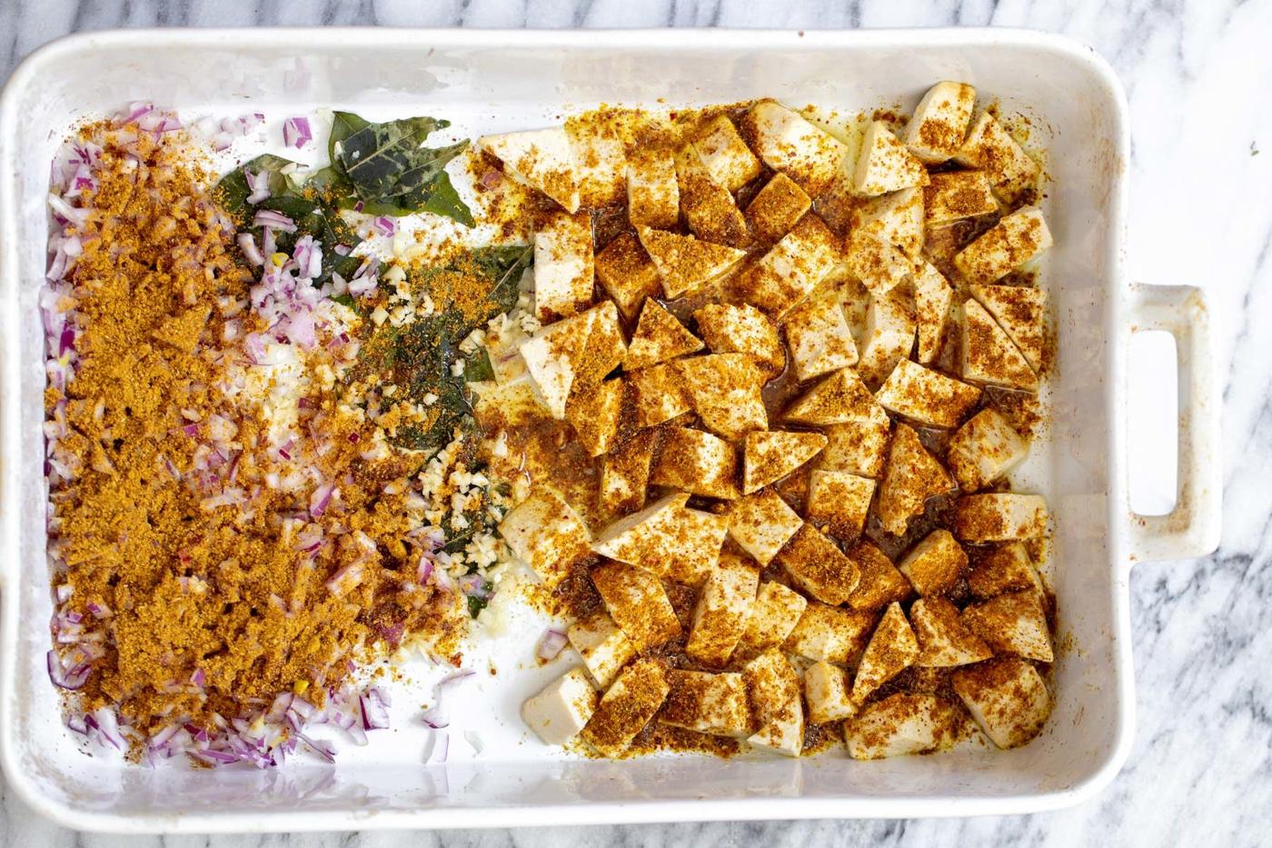 tofu, onions and curry leaves in a casserole dish sprinkled with madras curry powder