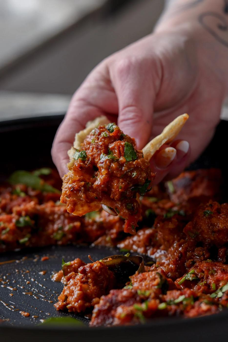 hand scooping up Madurai Chicken Curry with a piece of flatbread