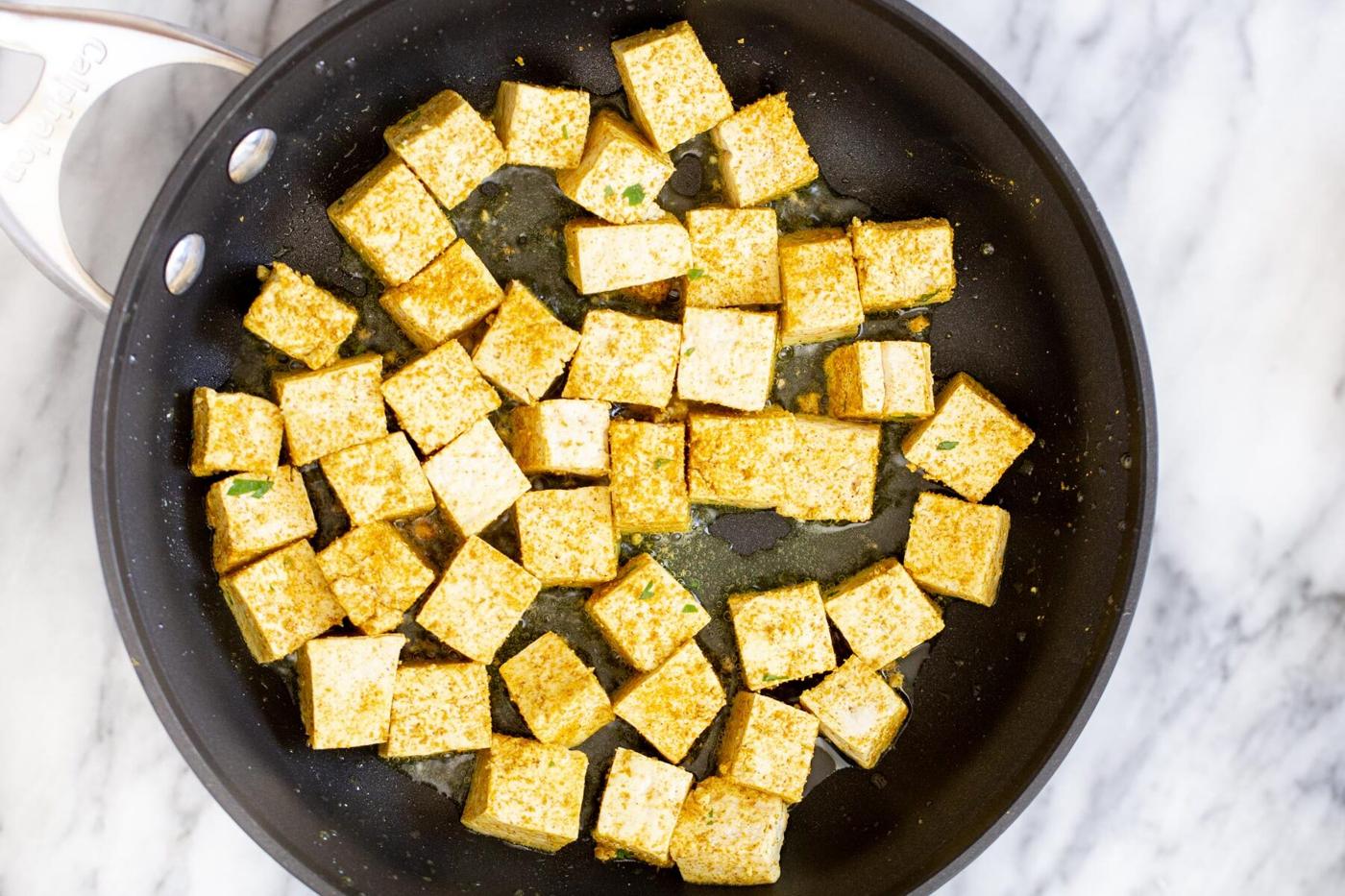 tofu cubes being fried in a sauteeing pan
