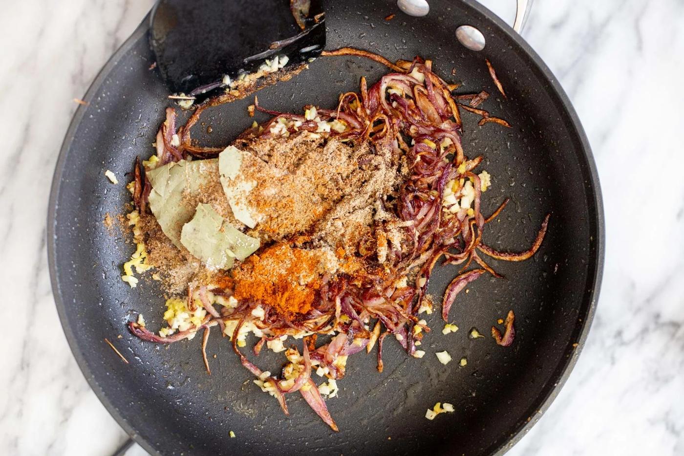 onion and garlic being tempered with spices in a black skillet