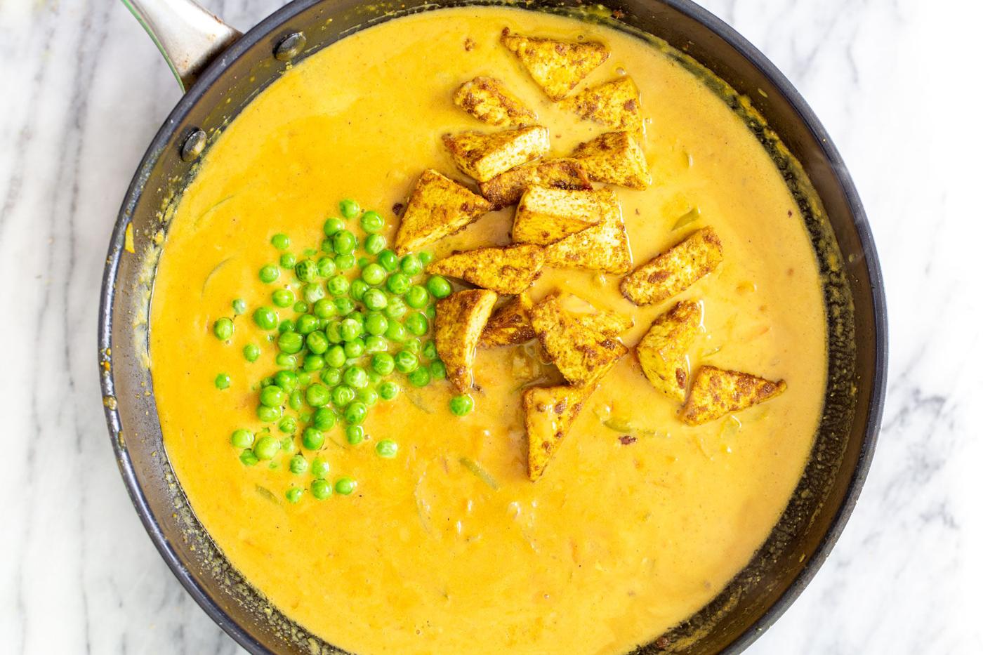 crispy tofu and peas being added to a sauteeing pan with coconut curry