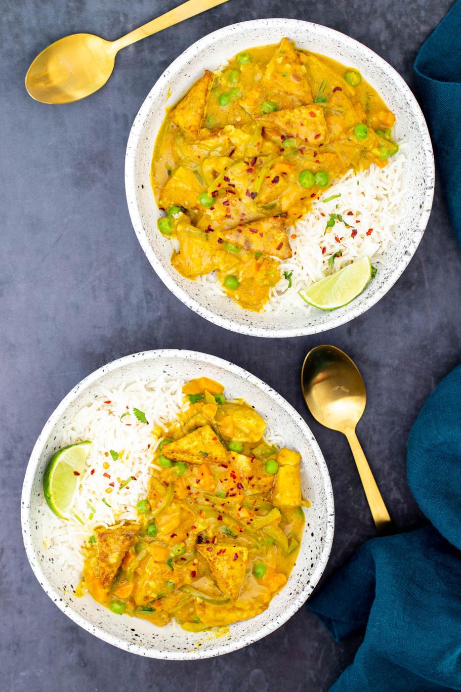 two bowls with rice and malaysian coconut tofu curry served with two golden spoons