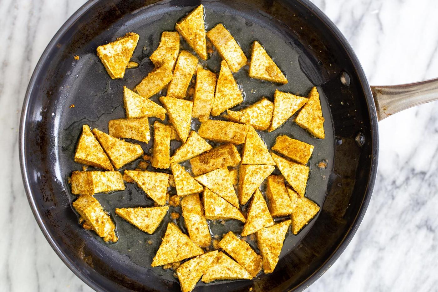 marinated tofu frying in a black sauteeing pan