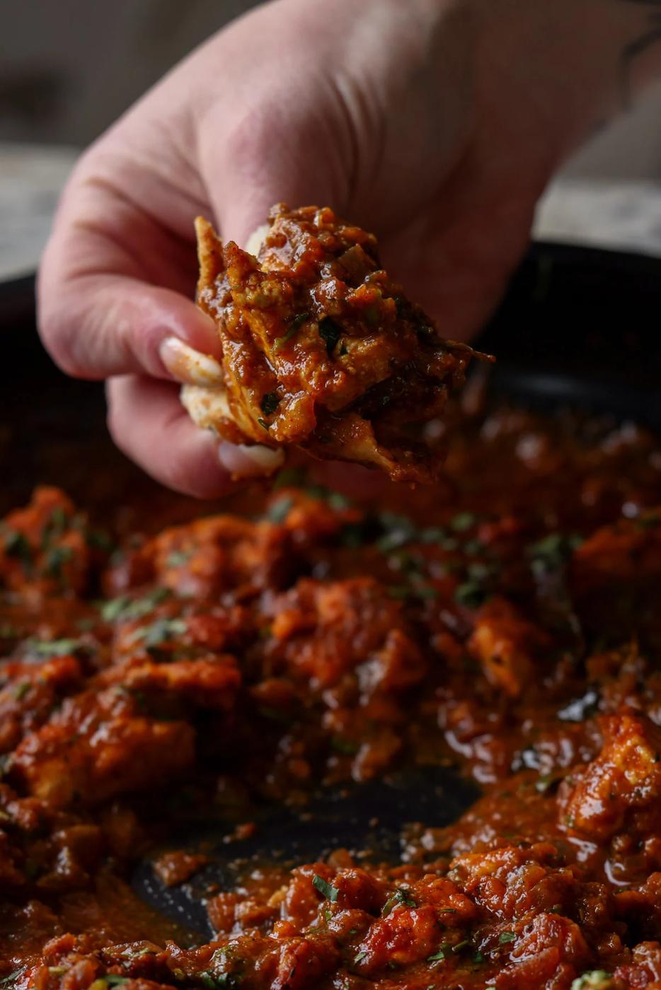 hand scooping up some malvani chicken curry using a piece of flatbread