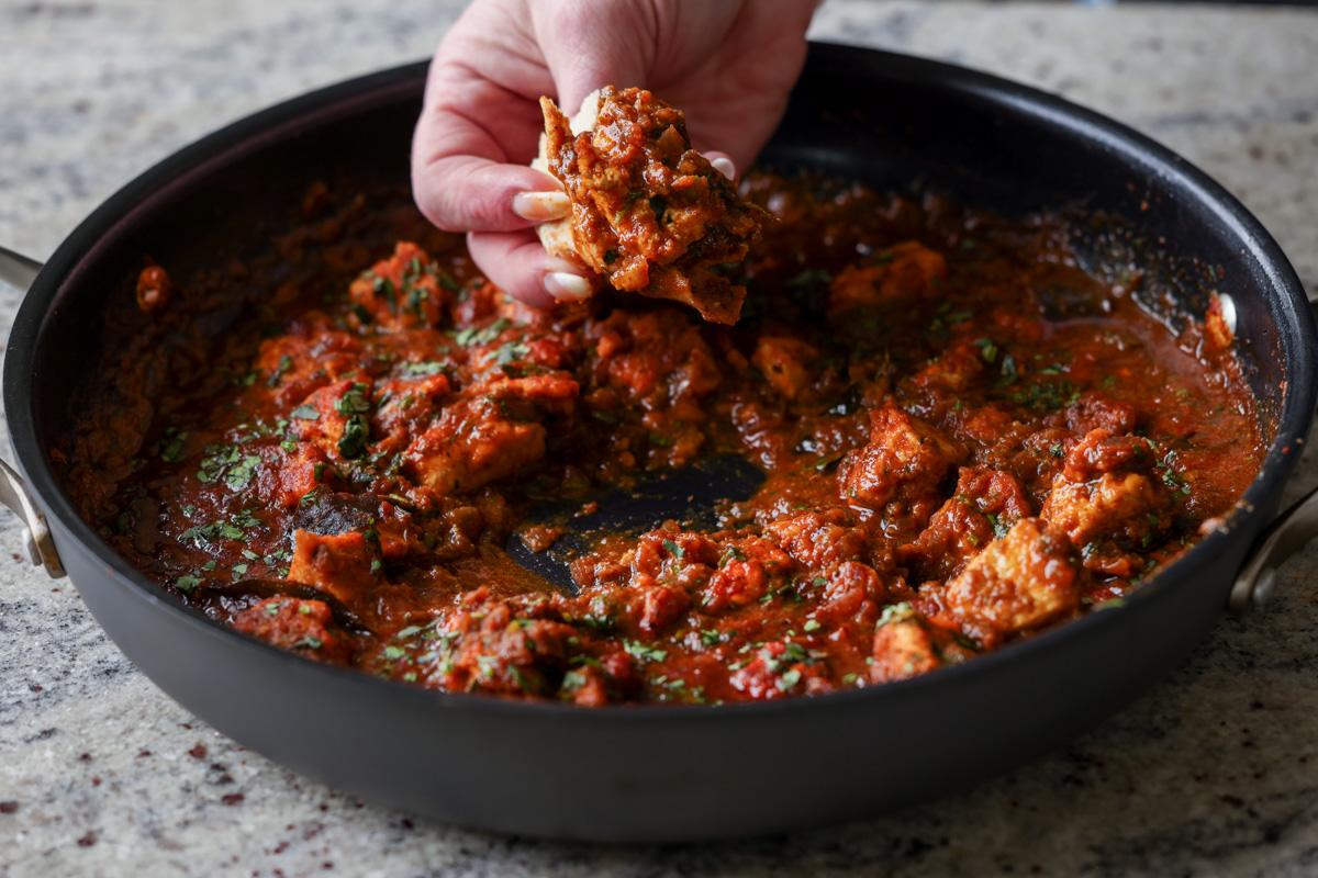 hand scooping up some malvani chicken curry using a piece of flatbread