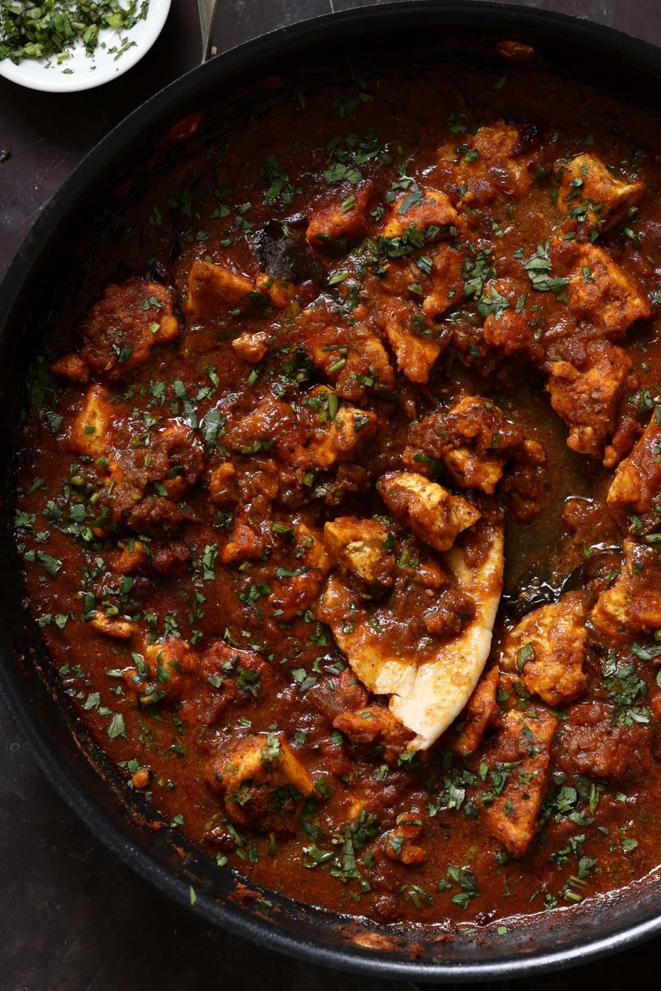malvani chicken curry in the pan with a piece of flatbread