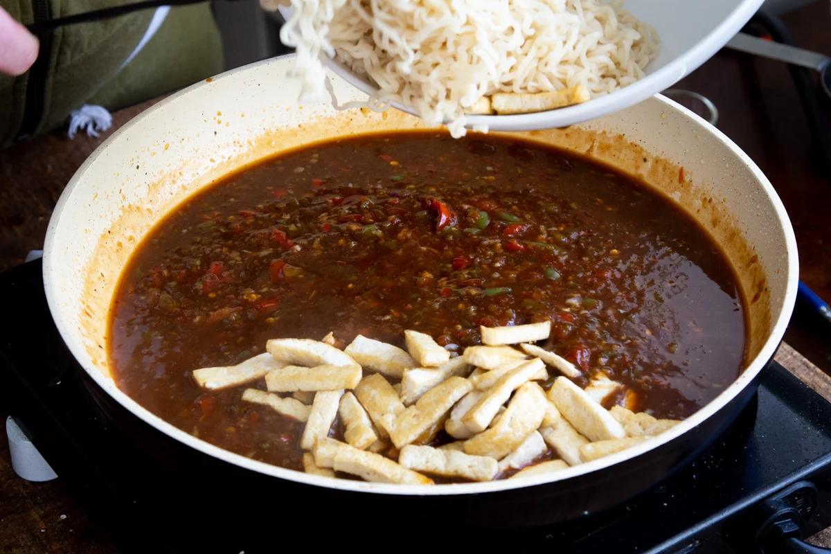noodles and fried tofu being added to a saucepan with Manchurian Sauce