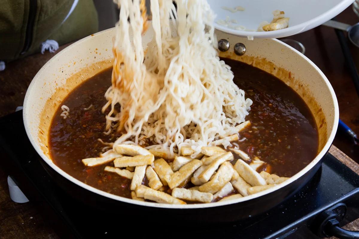 noodles being added to saucepan with Manchurian sauce and tofu