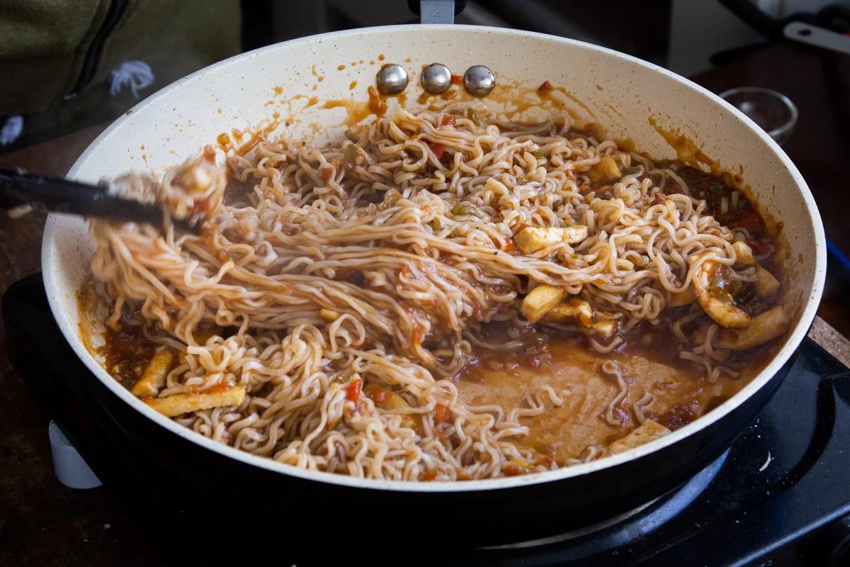 noodles being tossed with manchurian sauce in a pan
