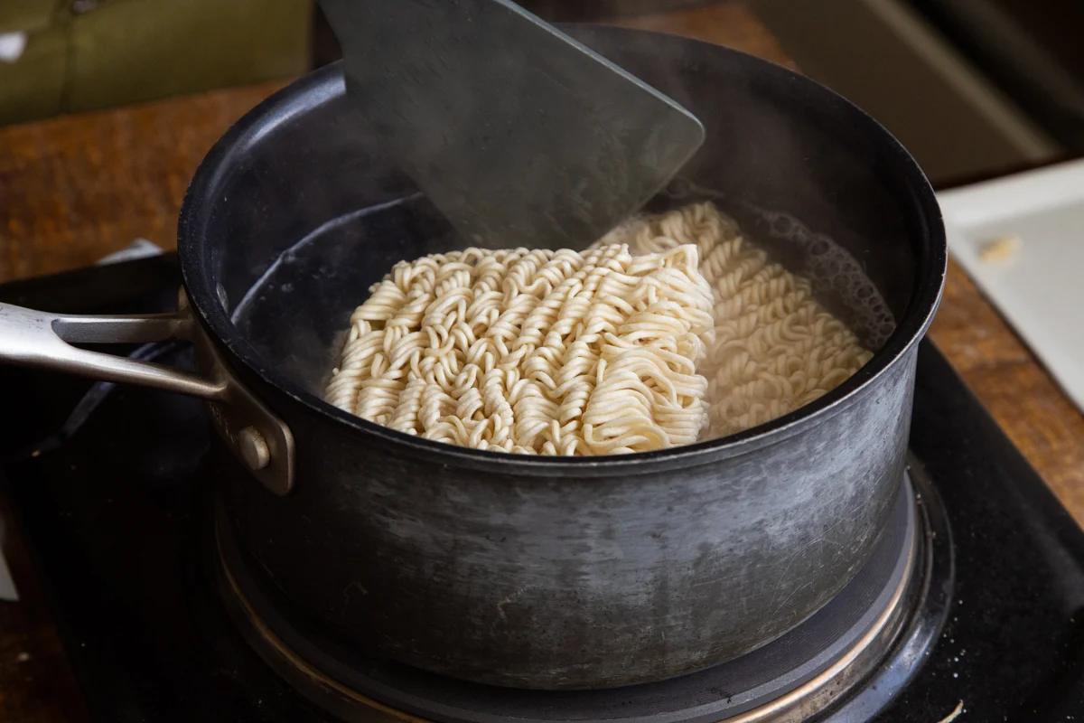 ramen noodles being cooked in a metal pot