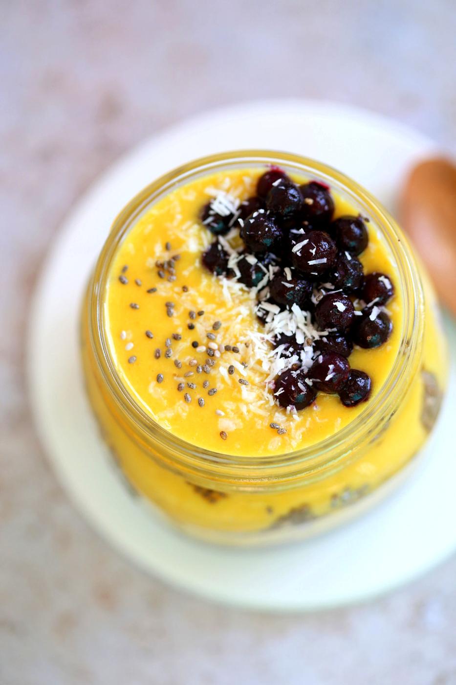 Vegan Mango Overnight Oats with Turmeric and Chia seeds in a glass jar, topped with wild bluerries