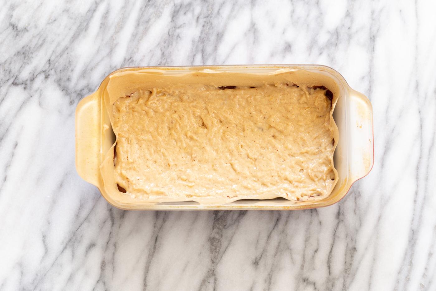 vanilla banana bread batter being scooped on top of dark batter to make marbled loaf