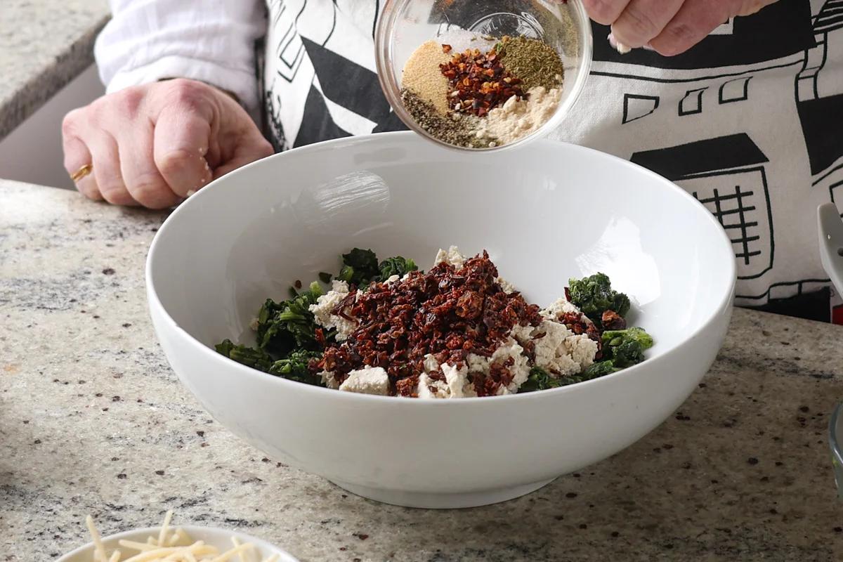 adding sun-dried tomato and spices to the bowl of spinach