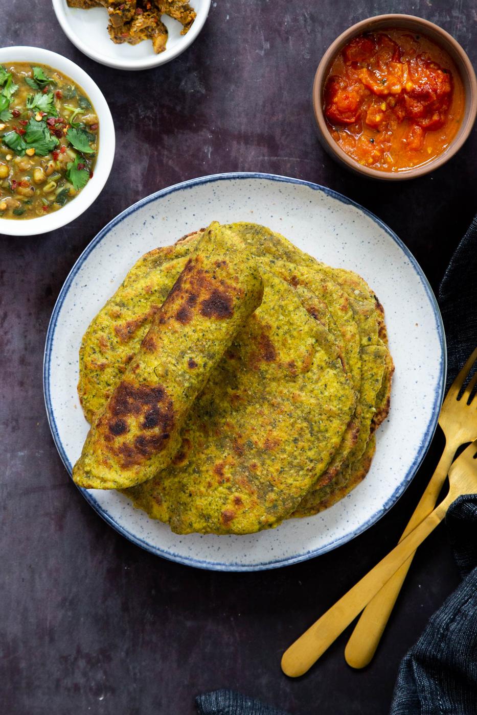 stacked masala parathas on a white plate with small side dishes on the side
