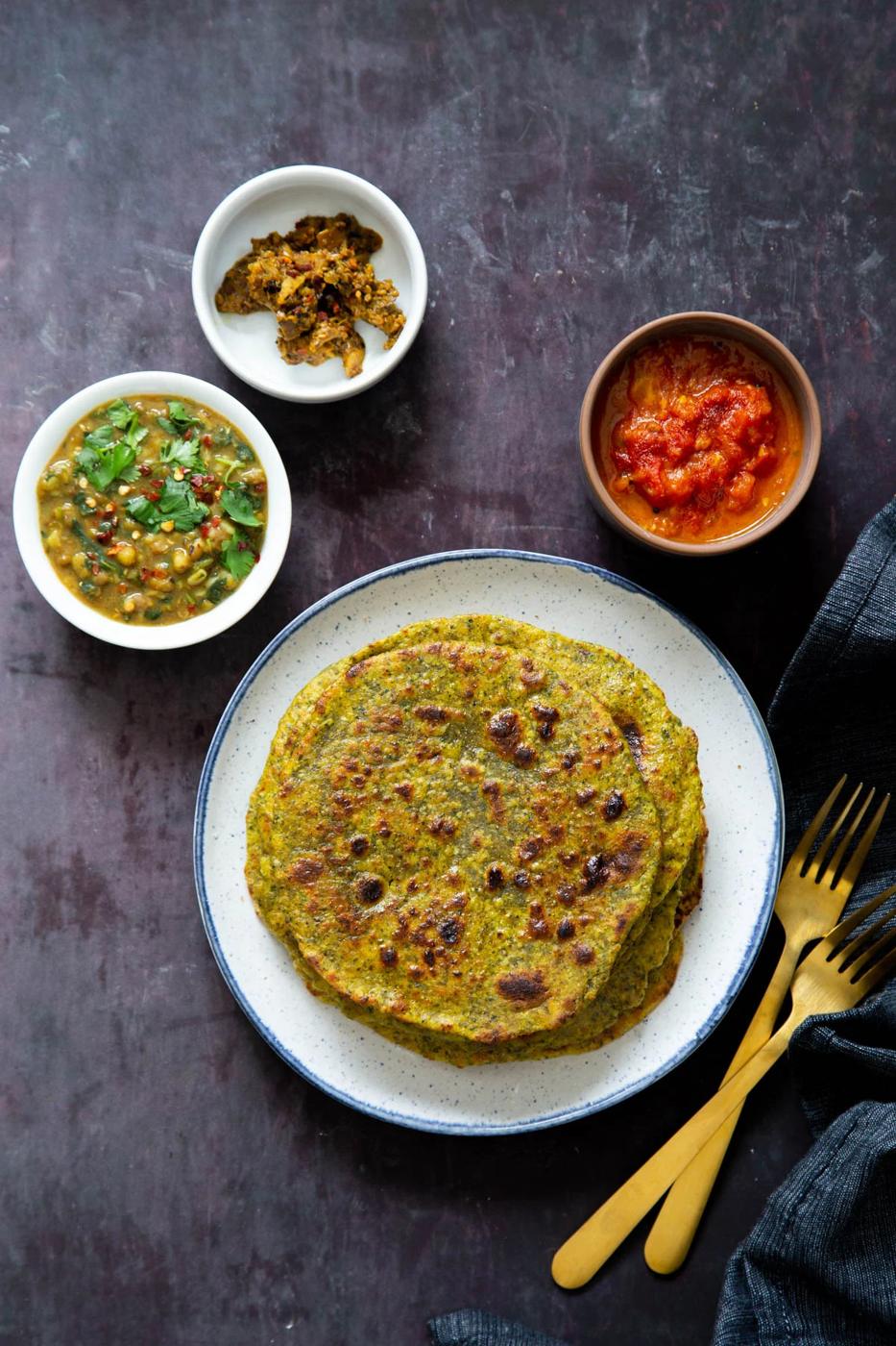 masala parathas on a plate and three small dishes with Indian chutneys