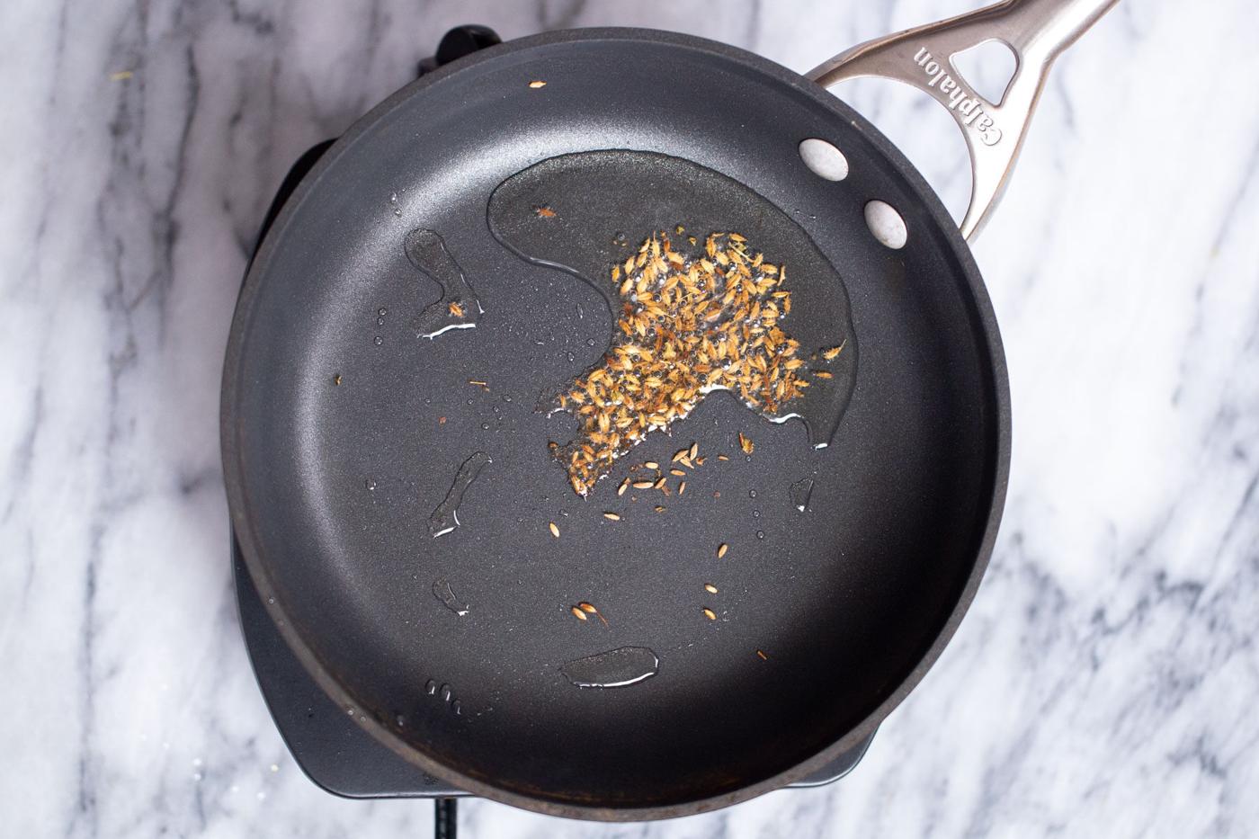 cumin seeds being added to hot oil in a sauteeing pan