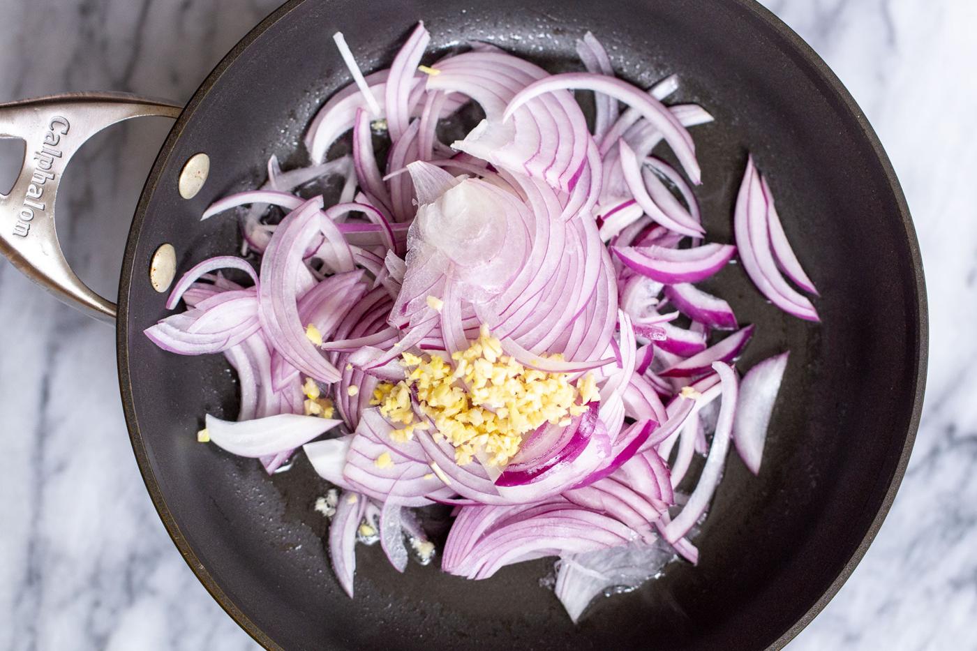 sliced red onions and ginger in a black sauteeing pan