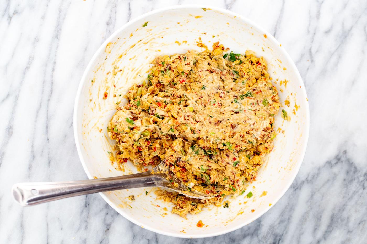 smashed chickpeas being mixed with veggies and lemon tahini dressing