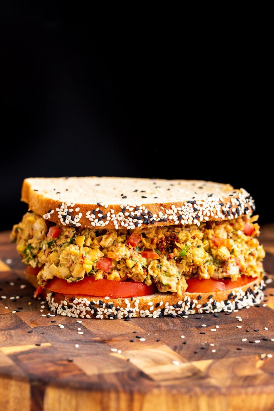 vegan Mediterranean chickpea salad sandwich on multigrain bread served on a wooden board