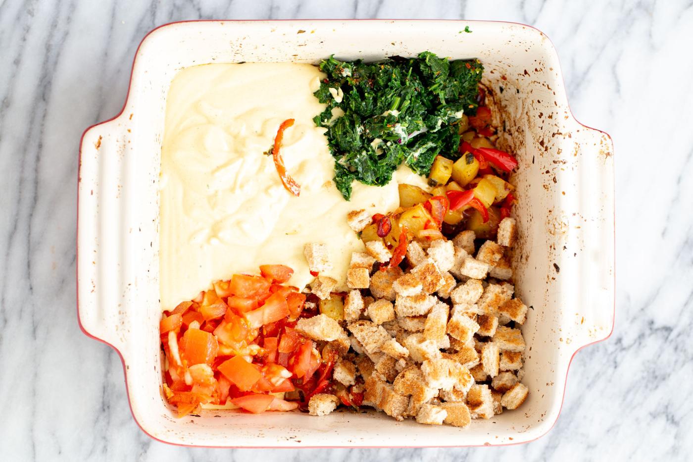 bread cubes, fresh spinach and tomatoes being added to egg casserole