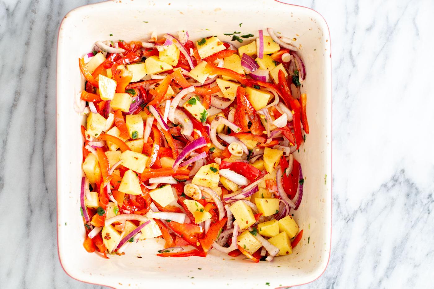 vegetables mixed with seasoning and oil in a white baking dish