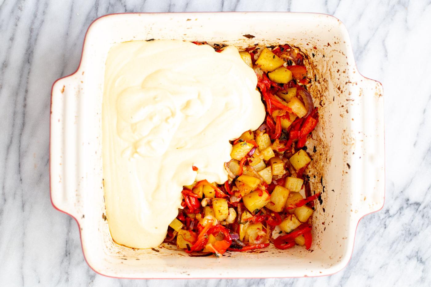 vegan egg mixture being poured on top of roasted vegetables in casserole dish to make egg casserole