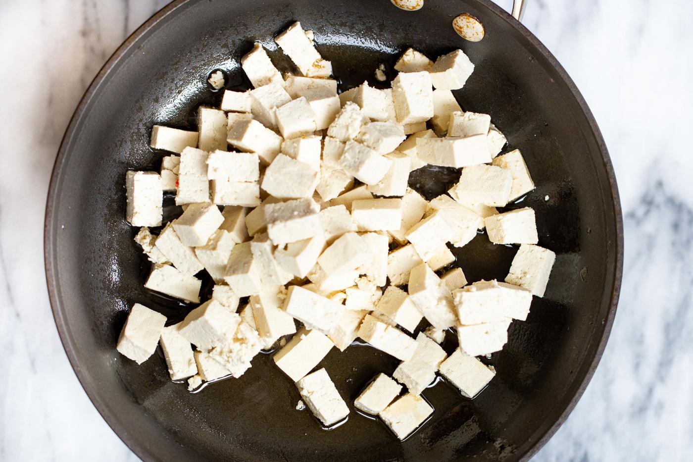tofu cubes frying in a black skillet