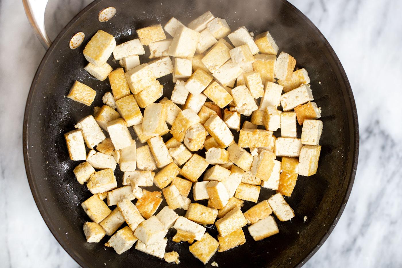 tofu cubes being fried in a black skillet