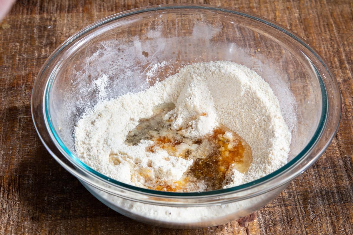 liquid ingredients being added to dry ingredients in a glass bowl