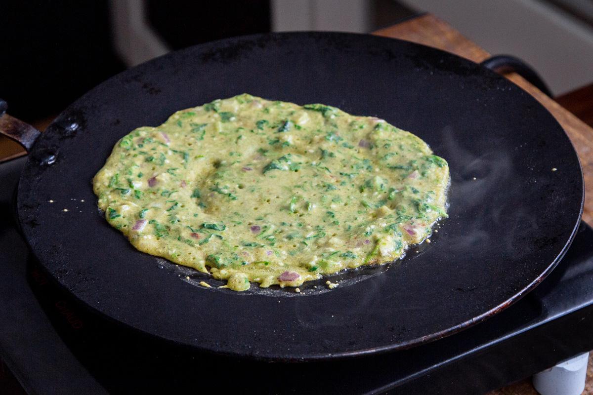 vegan lentil flour pancake with spinach frying in a black skillet