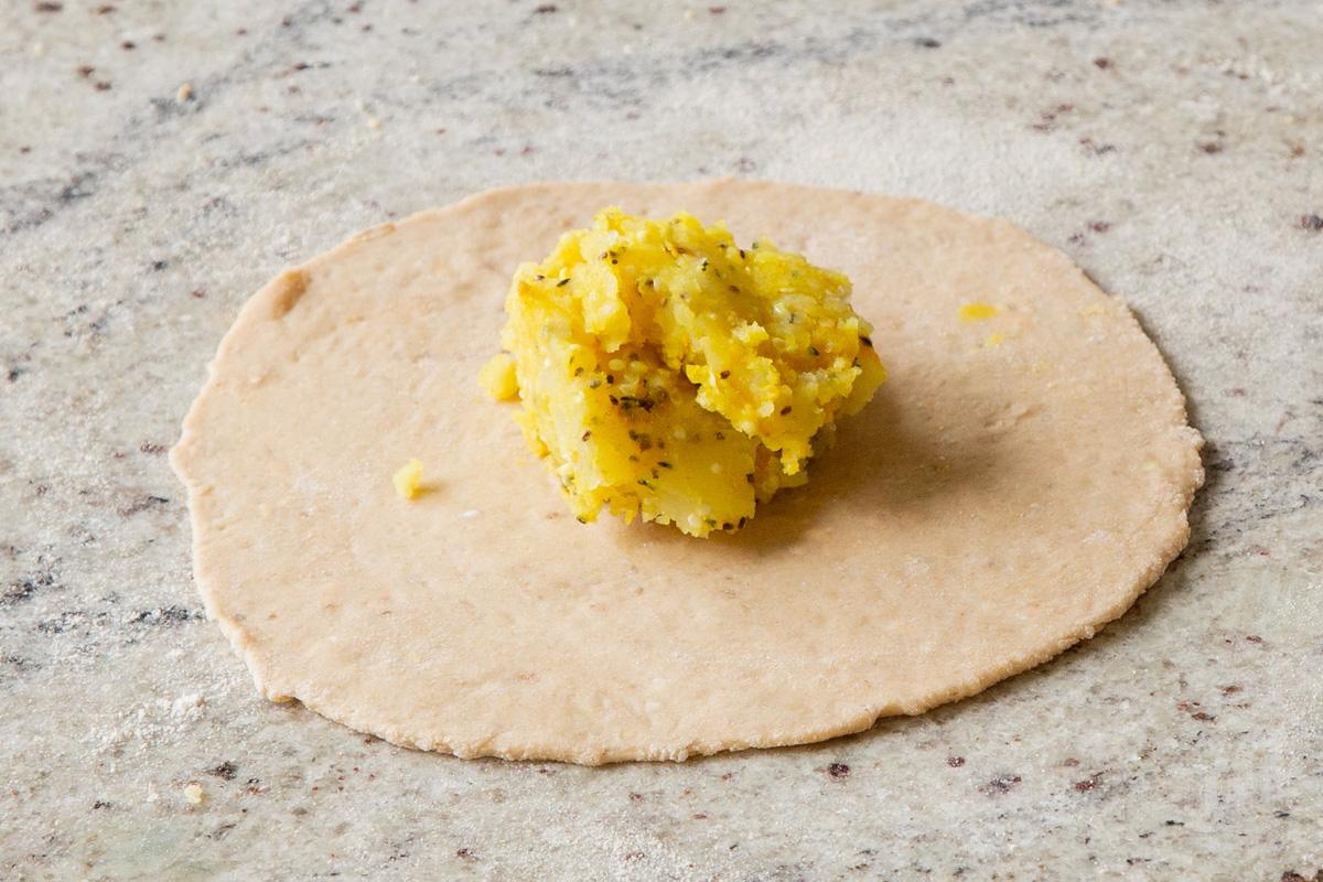 paratha dough rolled out on a lightly oiled countertop with potato filling in a pile in the center