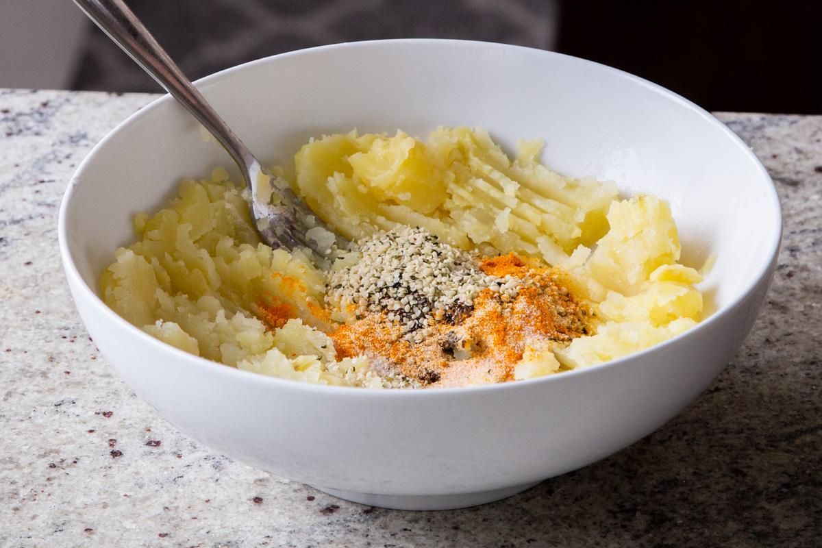 adding seeds and spices to the bowl of mashed potatoes