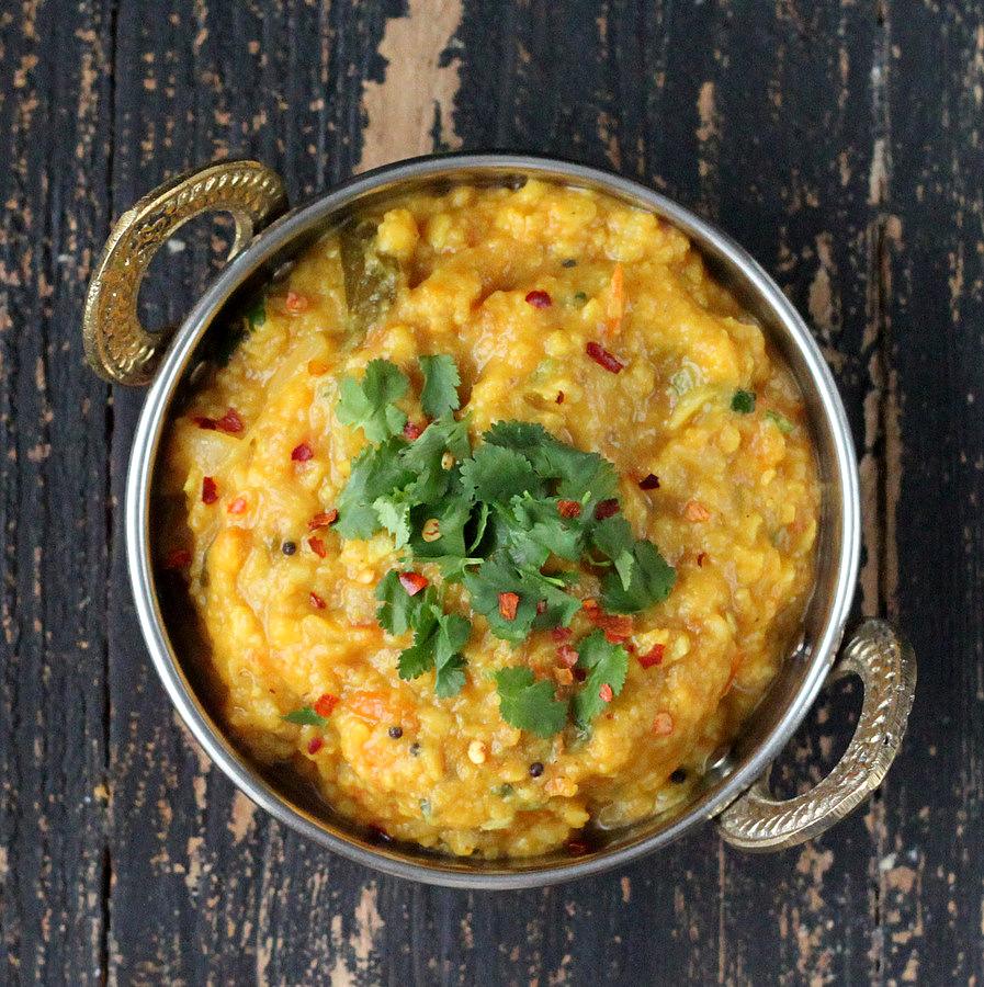 overhead shot of a bowl of Mung Dal (Moong Dal) and Split Pigeon Pea Stew topped with crushed red pepper and chopped herbs