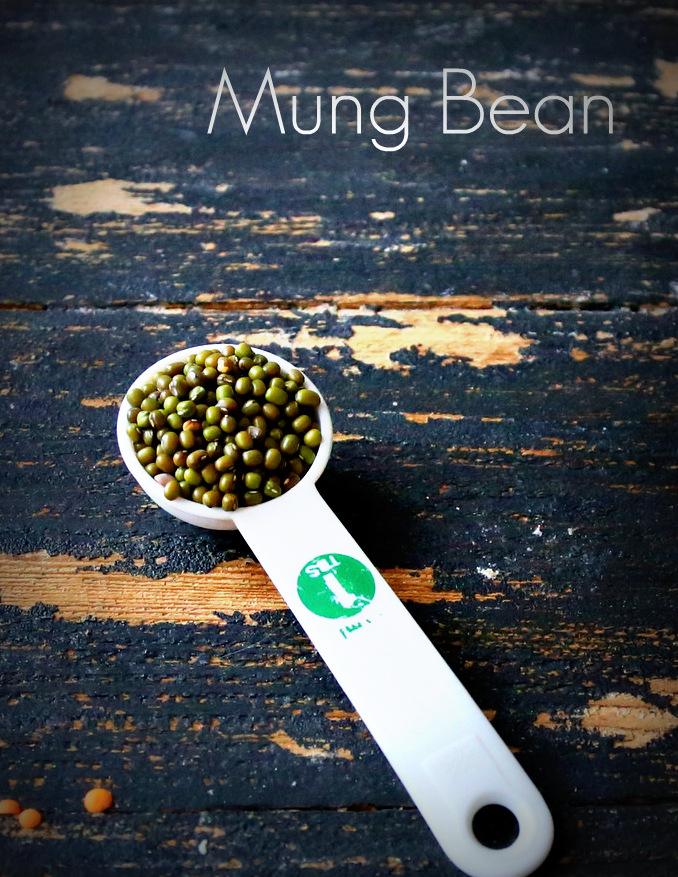 a white plastic teaspoon with mung beans on a black wooden table
