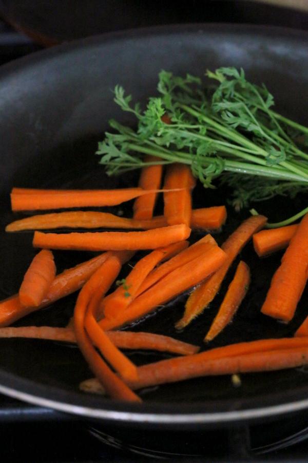carrot sticks and carrot greens sauteeing in a black pan