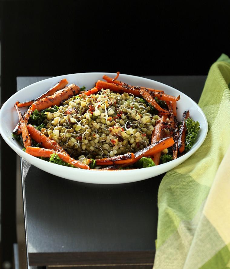 side view of a bowl of kale salad topped with sprouted mung beans and seared carrots