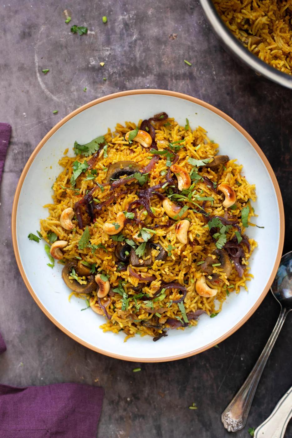 a plate with mushroom biryani topped with cashews and chopped cilantro