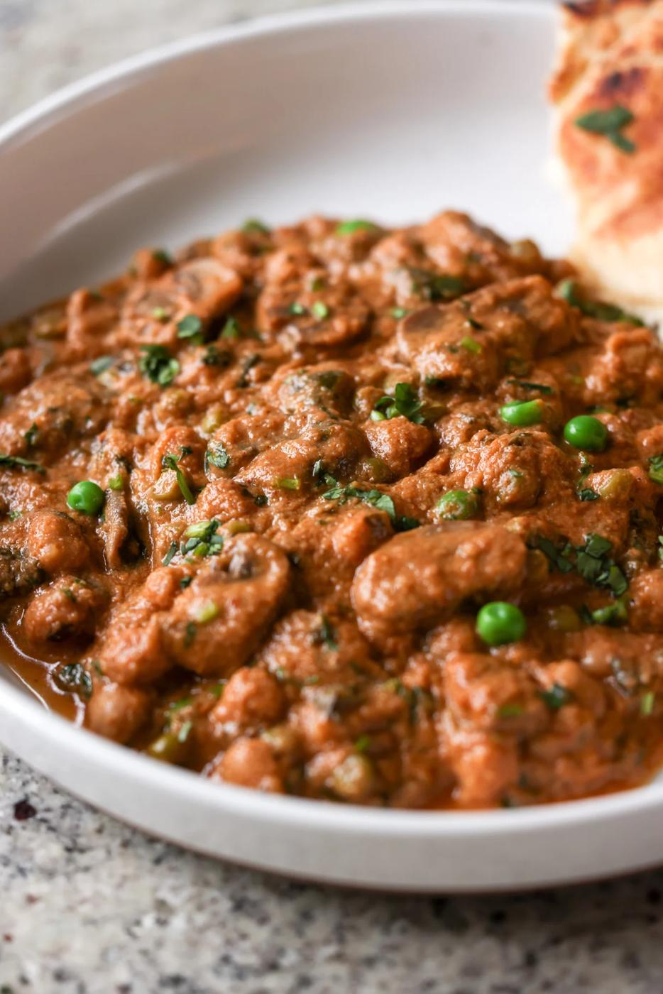 close-up of a bowl of mushroom matar masala with flatbread