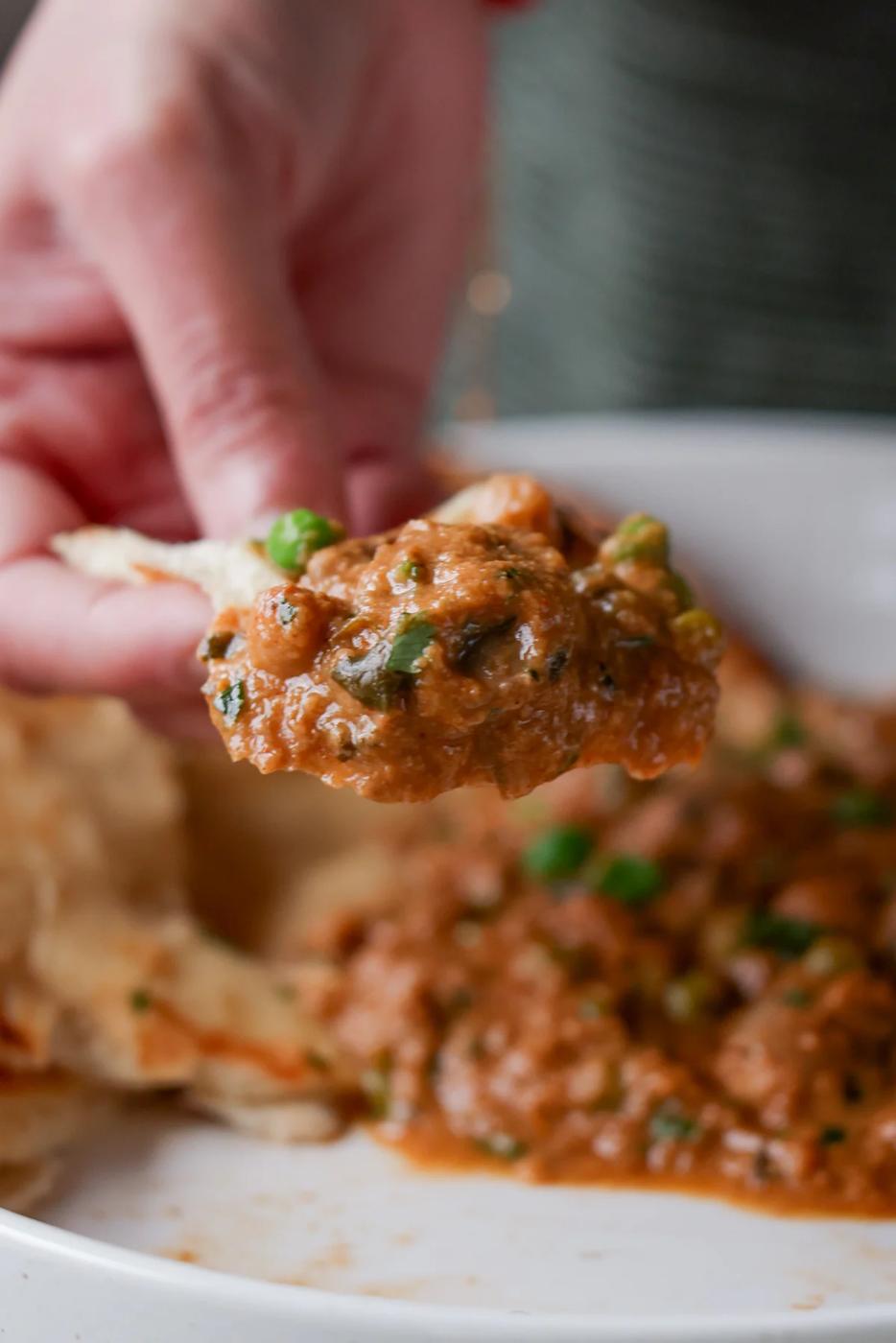 hand scooping up mushroom matar masala onto a piece of flatbread