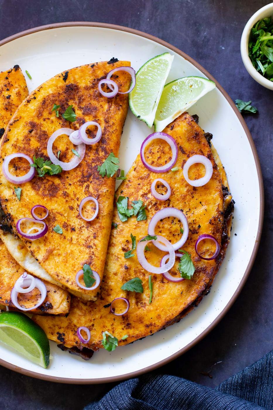 mushroom quesatacos on a plate with onions, cilantro, and lime