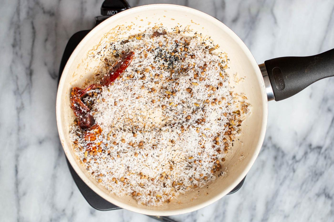 shredded coconut being added to a pan with toasted spices