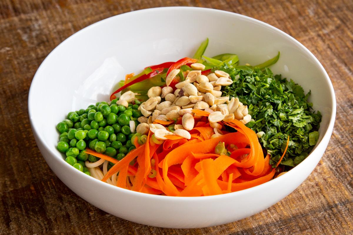 veggies and cooked spaghetti in a white bowl sprinkled with peanuts