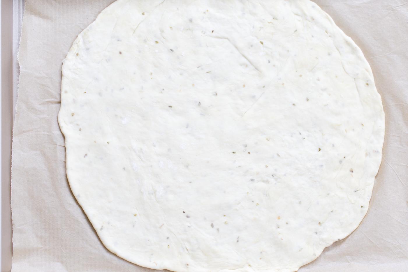 rolled out pizza dough on parchment paper