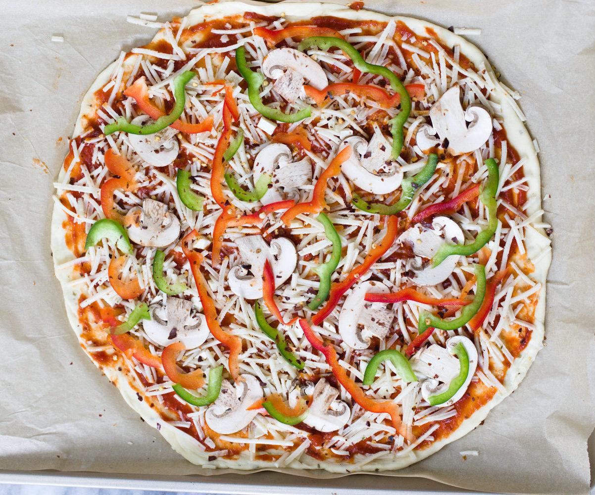 overhead shot of unbaked vegan pizza on a baking sheet topped with vegetables and vegan cheese shreds