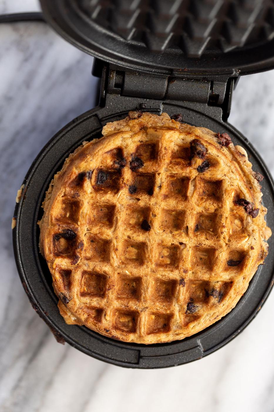 a vegan oatmeal chocolate chip waffle being baked in a black iron waffle maker