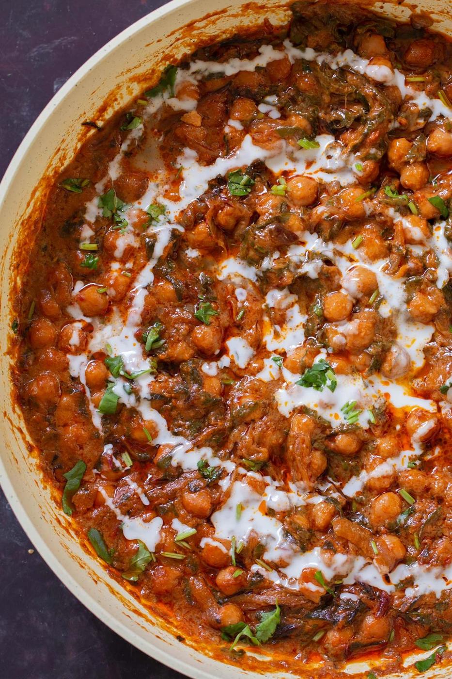 close-up of a panful of harissa chickpeas after cooking with cilantro garnish and coconut cream swirl