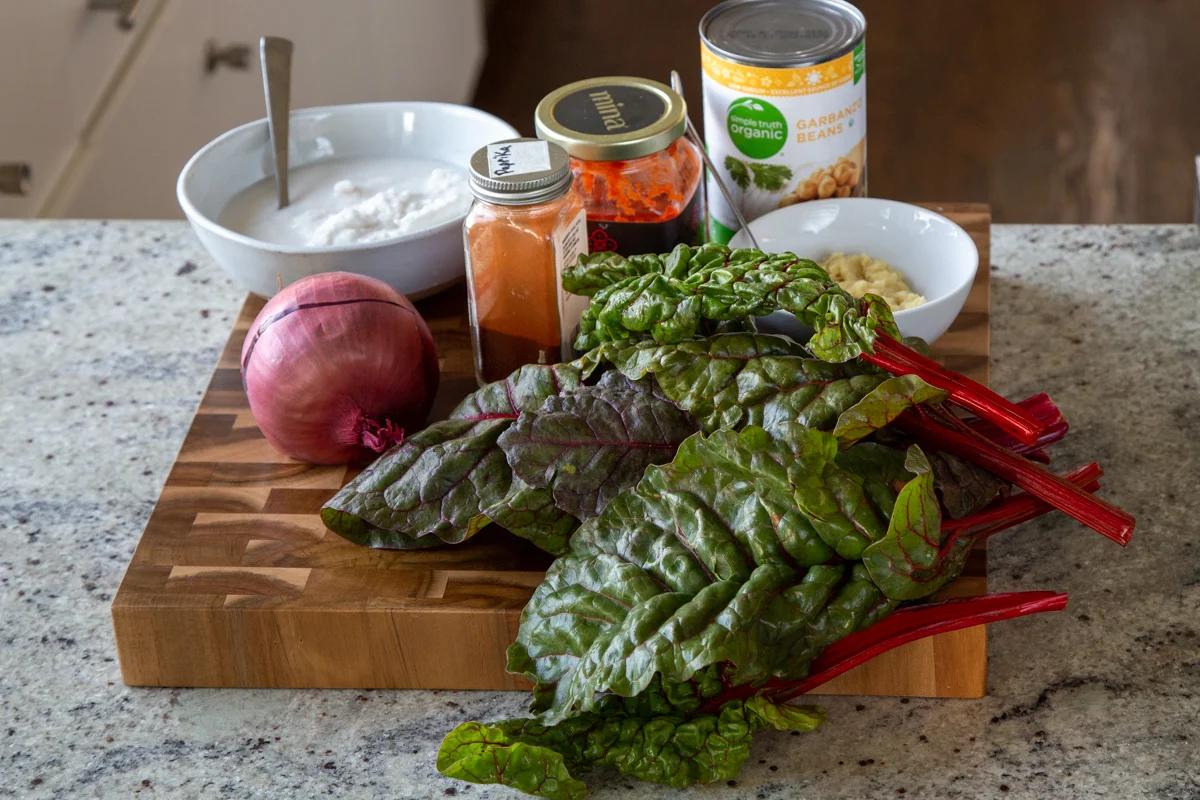chickpeas, greens, coconut milk, and seasonings on a wooden cutting board
