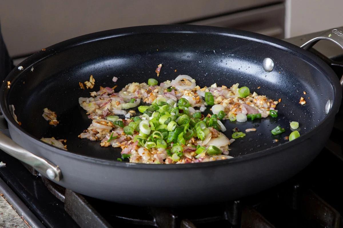 adding green onion to the pan of cooked garlic and onions