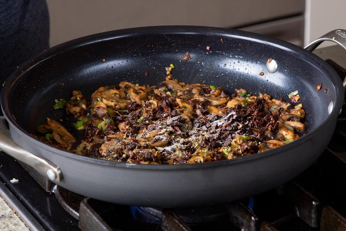 adding sun-dried tomato and spices to the pan of cooked mushrooms