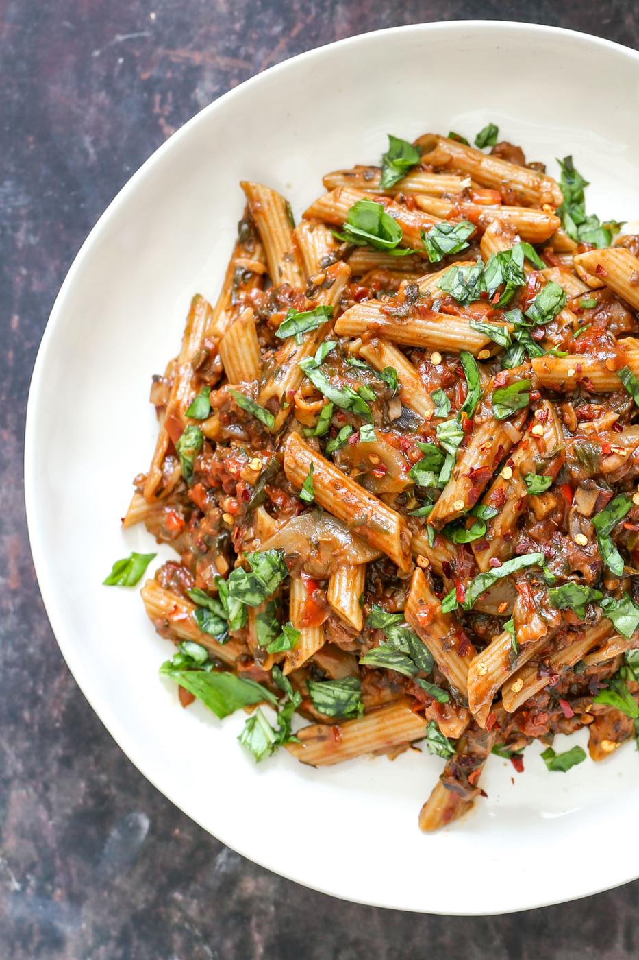 a white plate with penne with walnut sun-dried tomato sauce and fresh basil